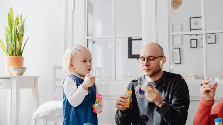 A joyful moment between a father and daughter blowing bubbles indoors, highlighting family fun.