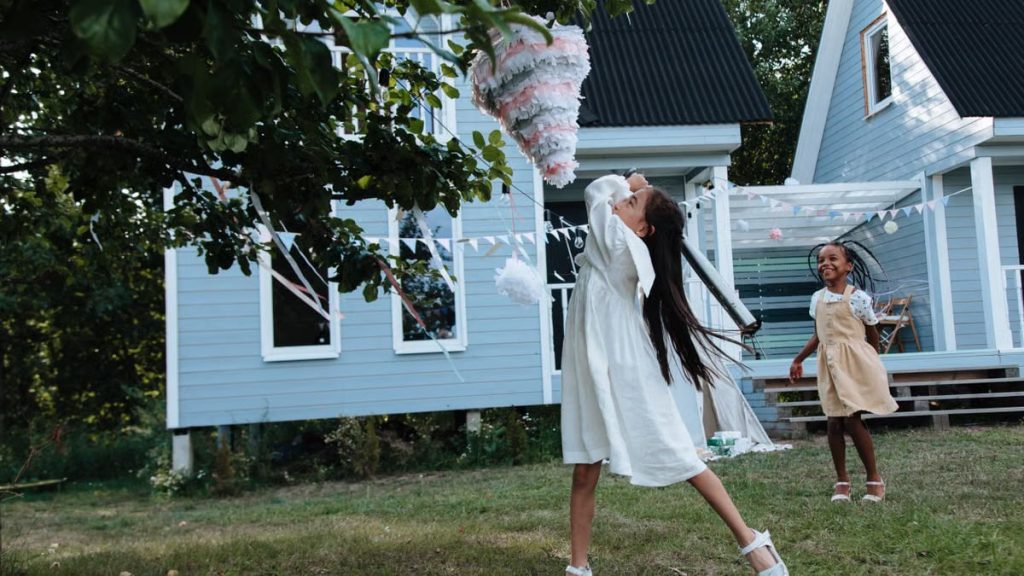 Kids enjoy an outdoor birthday party hitting a piñata in a backyard garden.